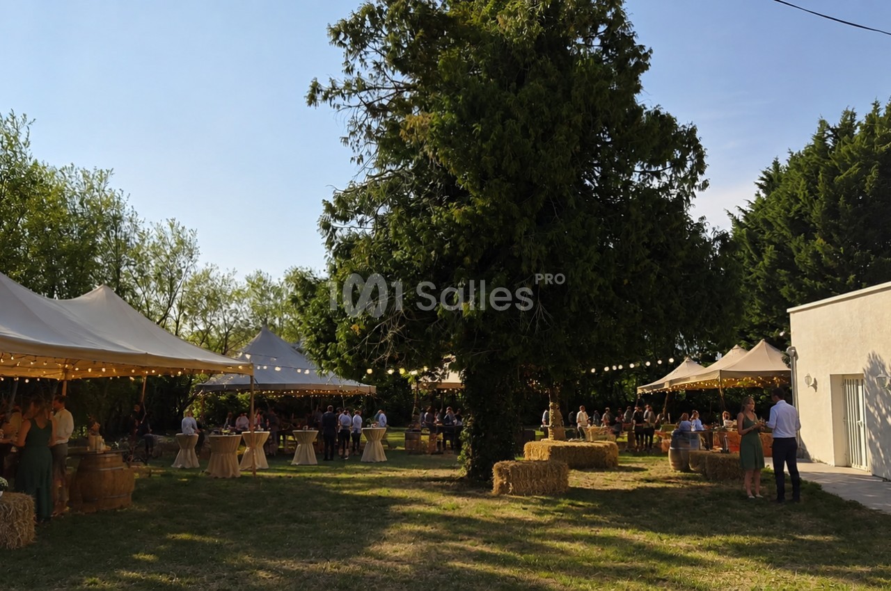 Jardin avec des tentes blanches, des tables décorées et des bottes de paille, lors d'un événement en plein air.