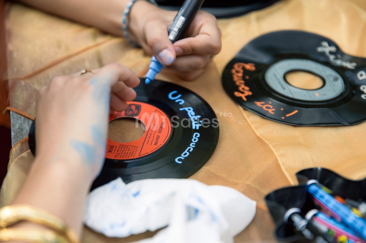 Personne écrivant au marqueur bleu sur un disque vinyle posé sur une table avec des crayons et des tissus.