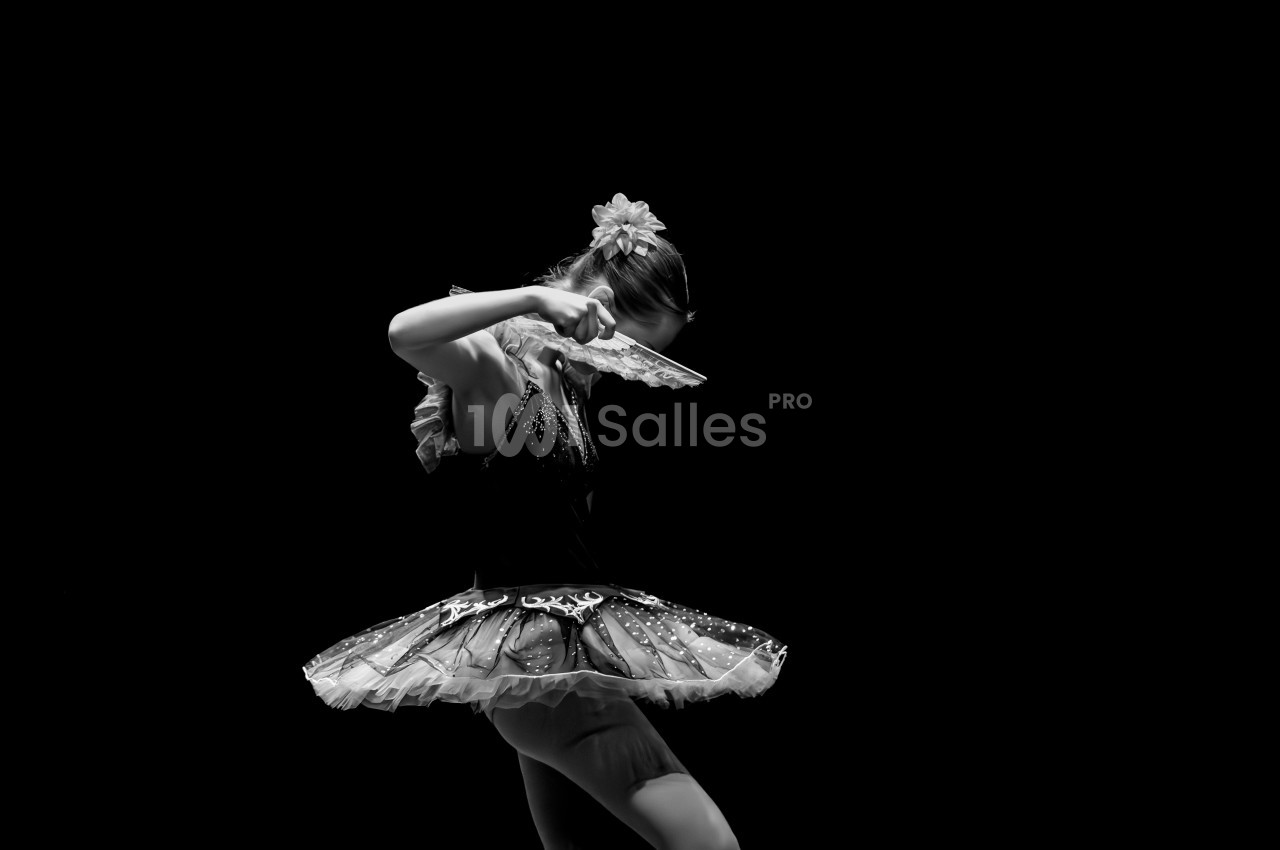 Danseuse en tutu exécutant un mouvement gracieux avec un éventail, éclairée sur fond noir.