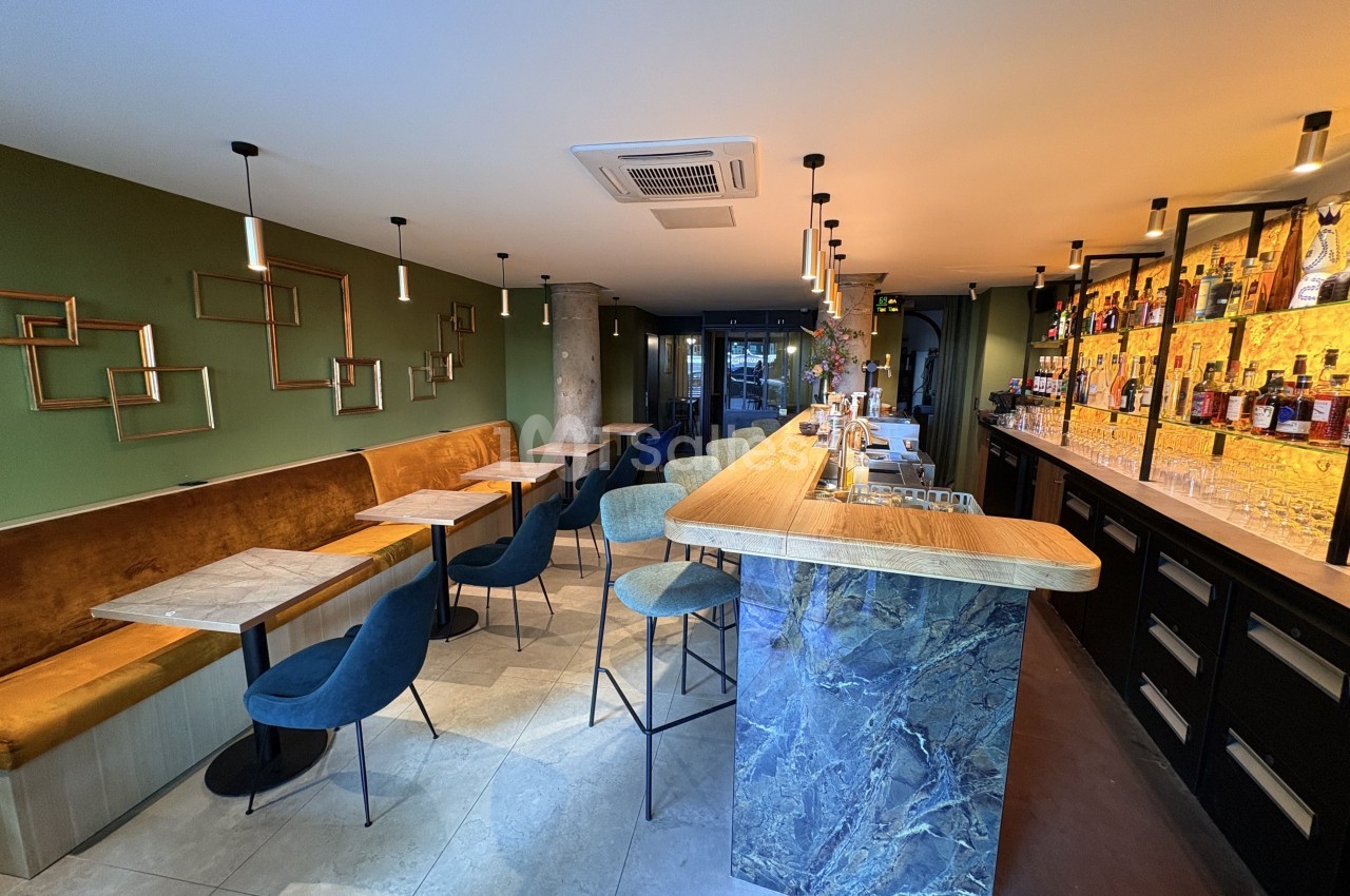 Intérieur d'un bar moderne avec comptoir en marbre, banquettes, chaises et étagères de bouteilles illuminées.