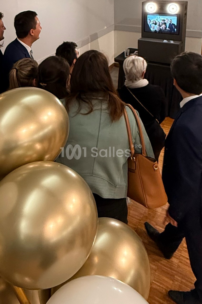 Un groupe de personnes regarde un écran affichant une photo, près d'une décoration avec des ballons dorés.