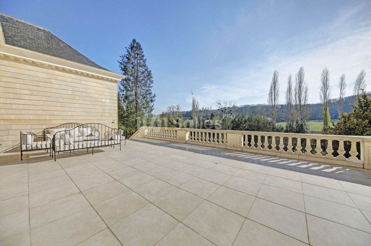 Grande terrasse en pierre avec balustrade, mobilier en fer forgé et vue dégagée sur un paysage arboré.