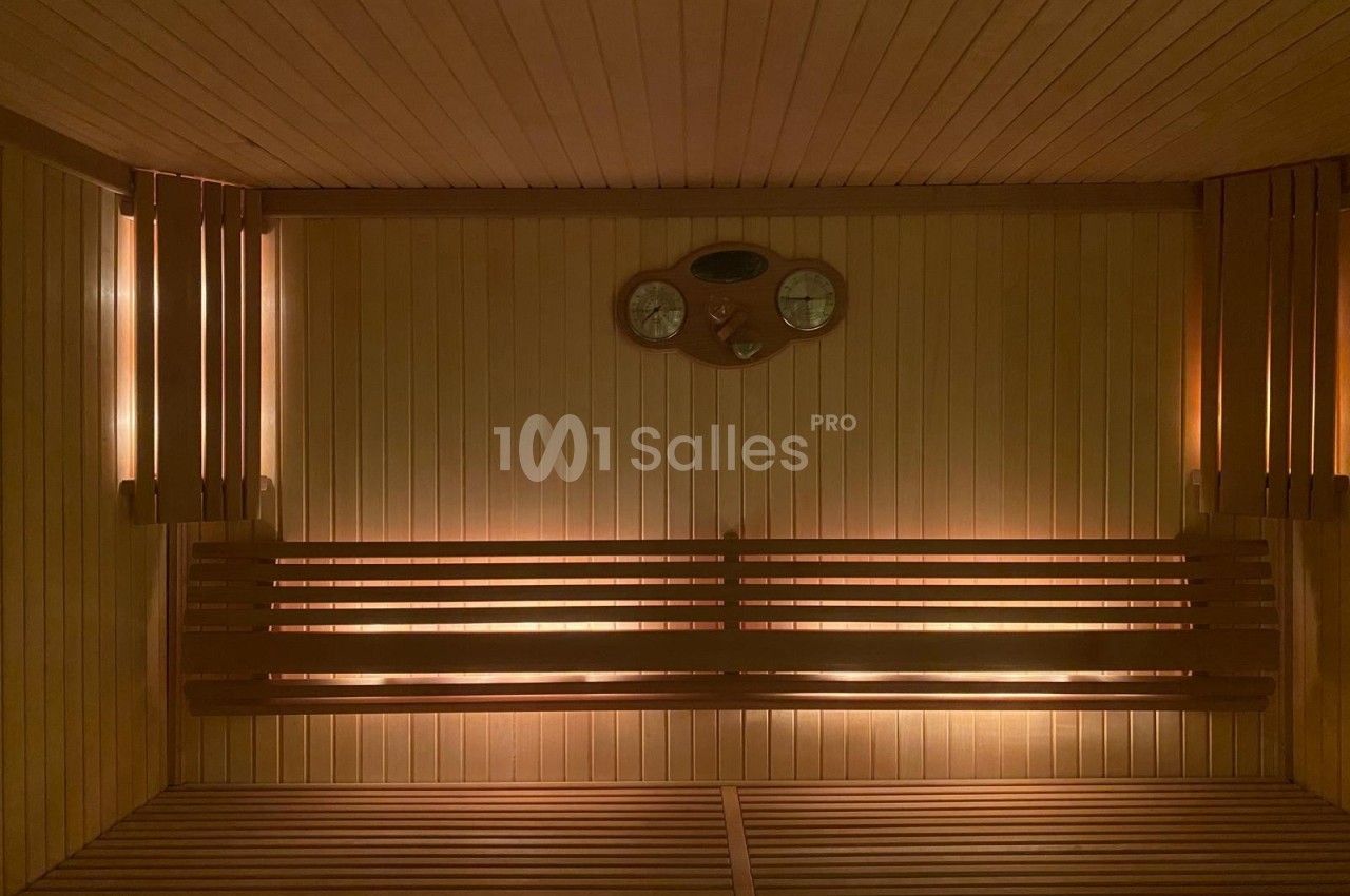 Intérieur d'un sauna en bois avec bancs, éclairage tamisé et thermomètre mural.