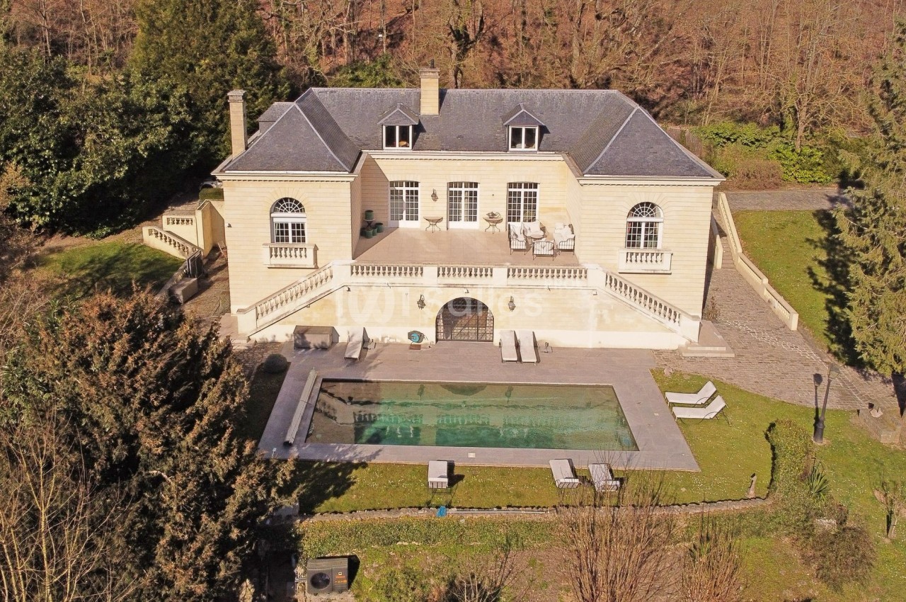 Vue aérienne d'une grande maison en pierre avec piscine, terrasse et jardin arboré en arrière-plan.
