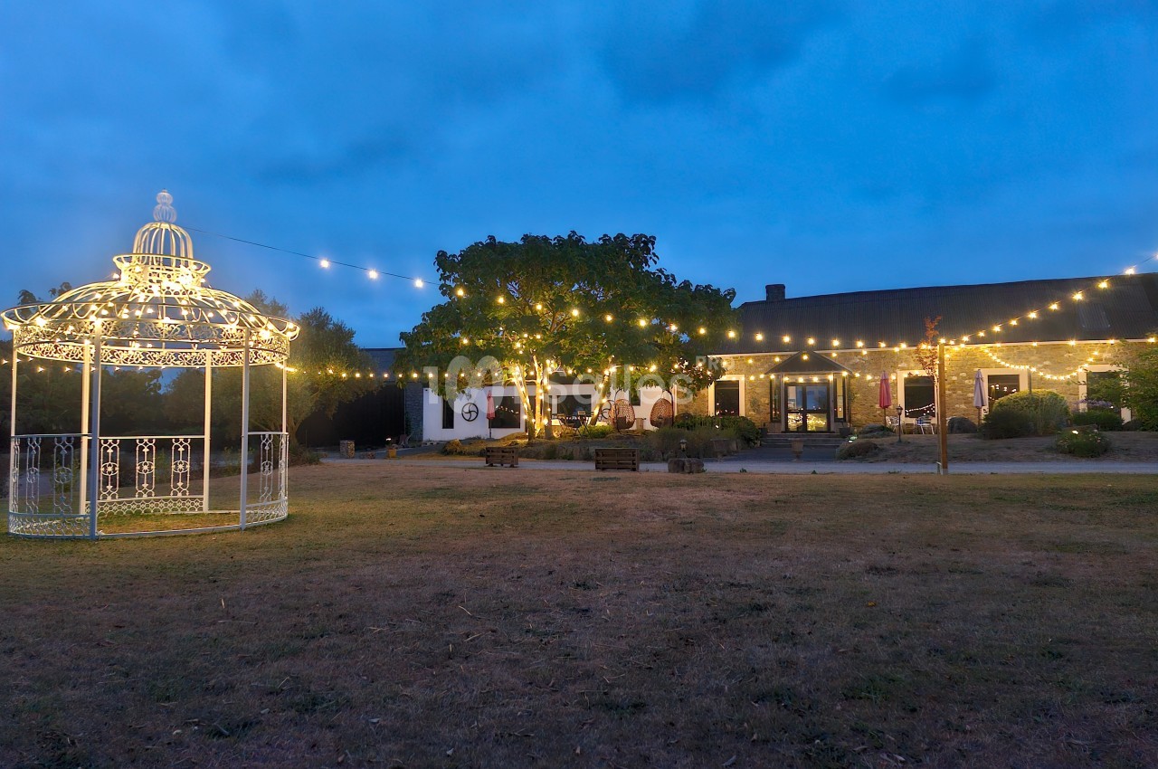 Jardin éclairé au crépuscule avec un kiosque illuminé et des guirlandes lumineuses suspendues devant un bâtiment.