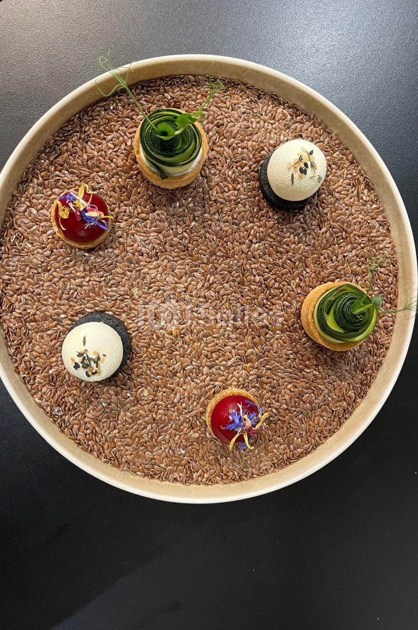 Assiette ronde garnie de riz complet avec six petits desserts disposés symétriquement - deux mousses blanches, deux tartelettes rouges et deux verrines vertes.