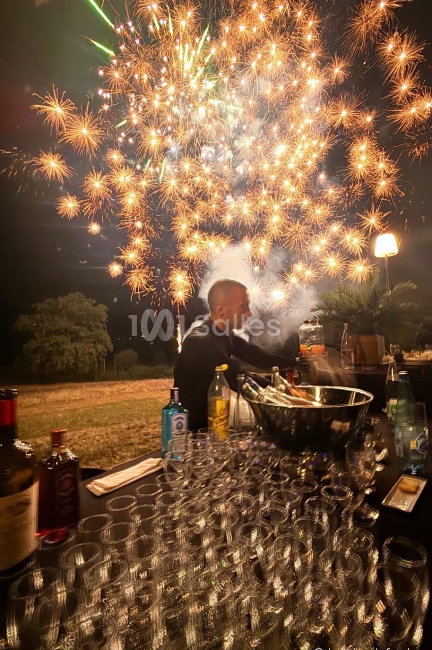 Feu d'artifice doré au-dessus d'une table dressée en plein air avec verres et bouteilles.