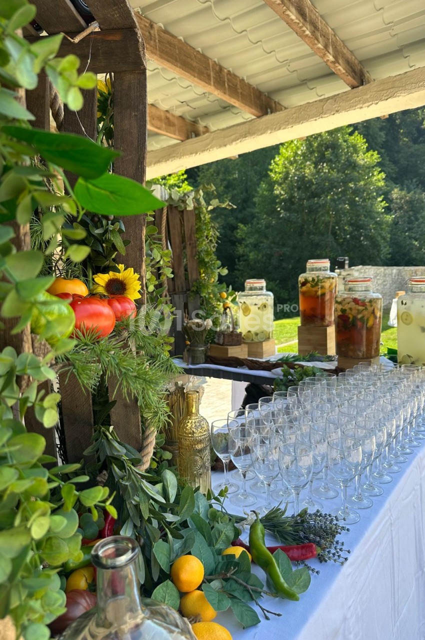 Terrasse couverte dressée pour réception - table blanche avec verres, jarres de boissons, fruits et fleurs frais.