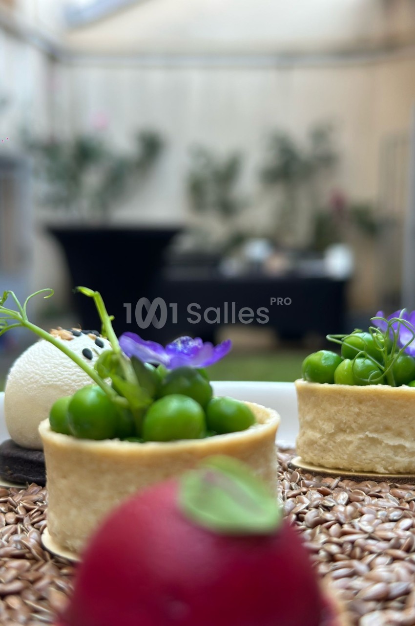 Petits canapés garnis de pois verts et fleur violette, sur tapis de gravier, intérieur flou.