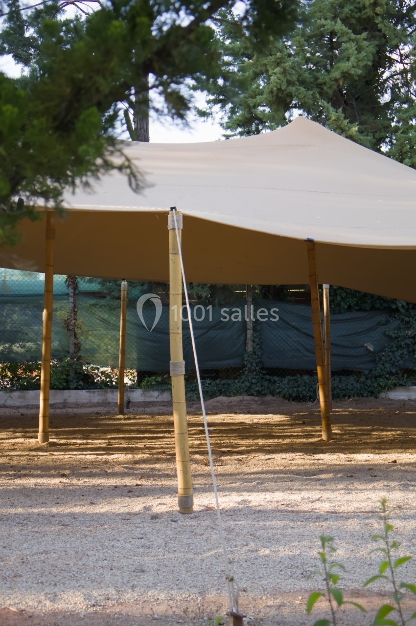 Tente beige en toile tendue sur des poteaux en bambou, installée dans un espace extérieur entouré de végétation.