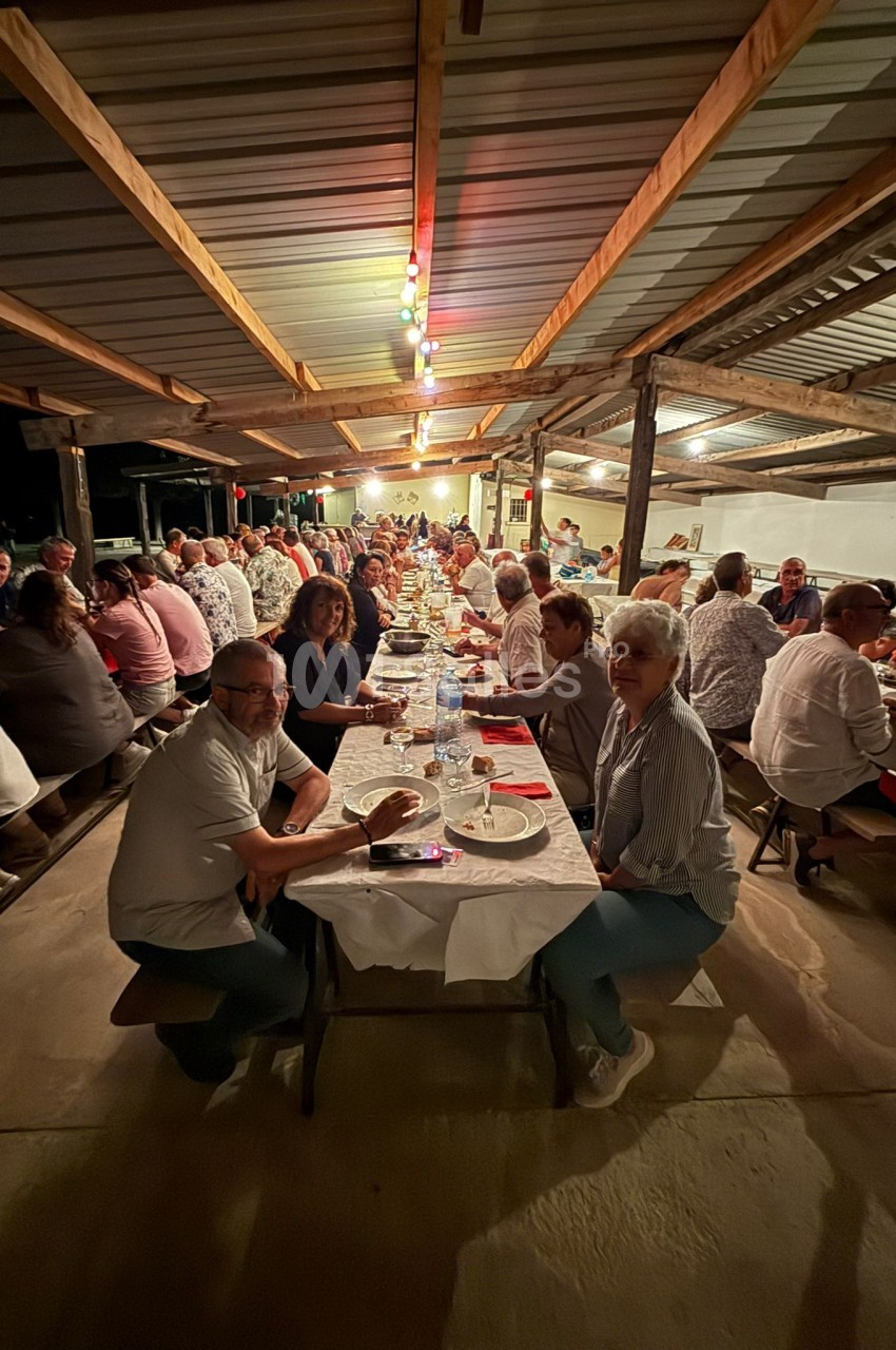 Des personnes assises à de longues tables sous un abri éclairé, partageant un repas convivial en soirée.