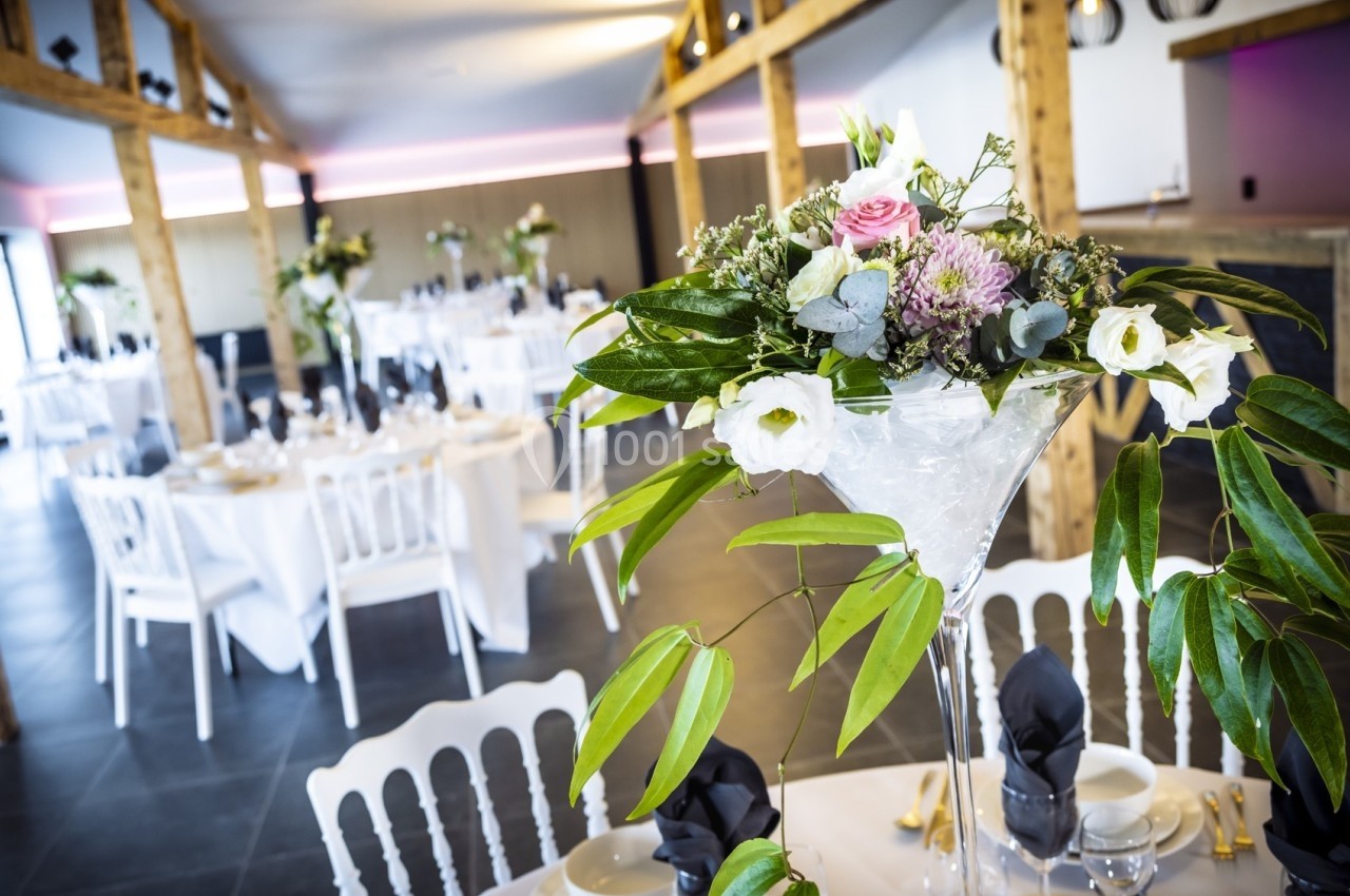Salle de réception décorée avec des tables dressées et des centres de table floraux dans un cadre lumineux.