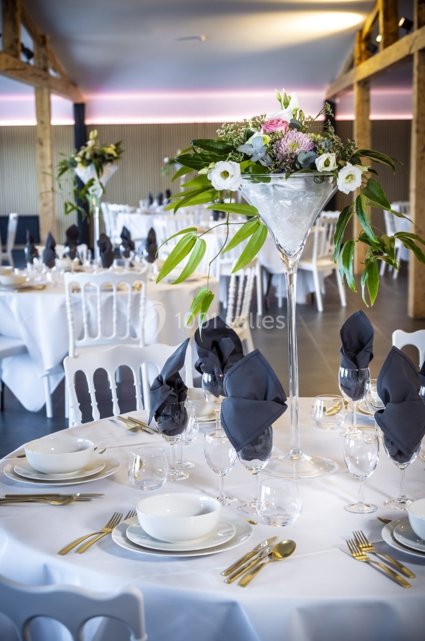 Salle de réception décorée avec des tables élégantes, nappes blanches, serviettes noires et centre de table floral.