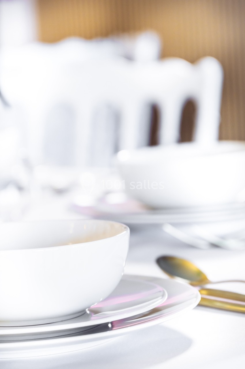 Deux assiettes blanches empilées avec des bols assortis sur une table dressée, éclairage lumineux.