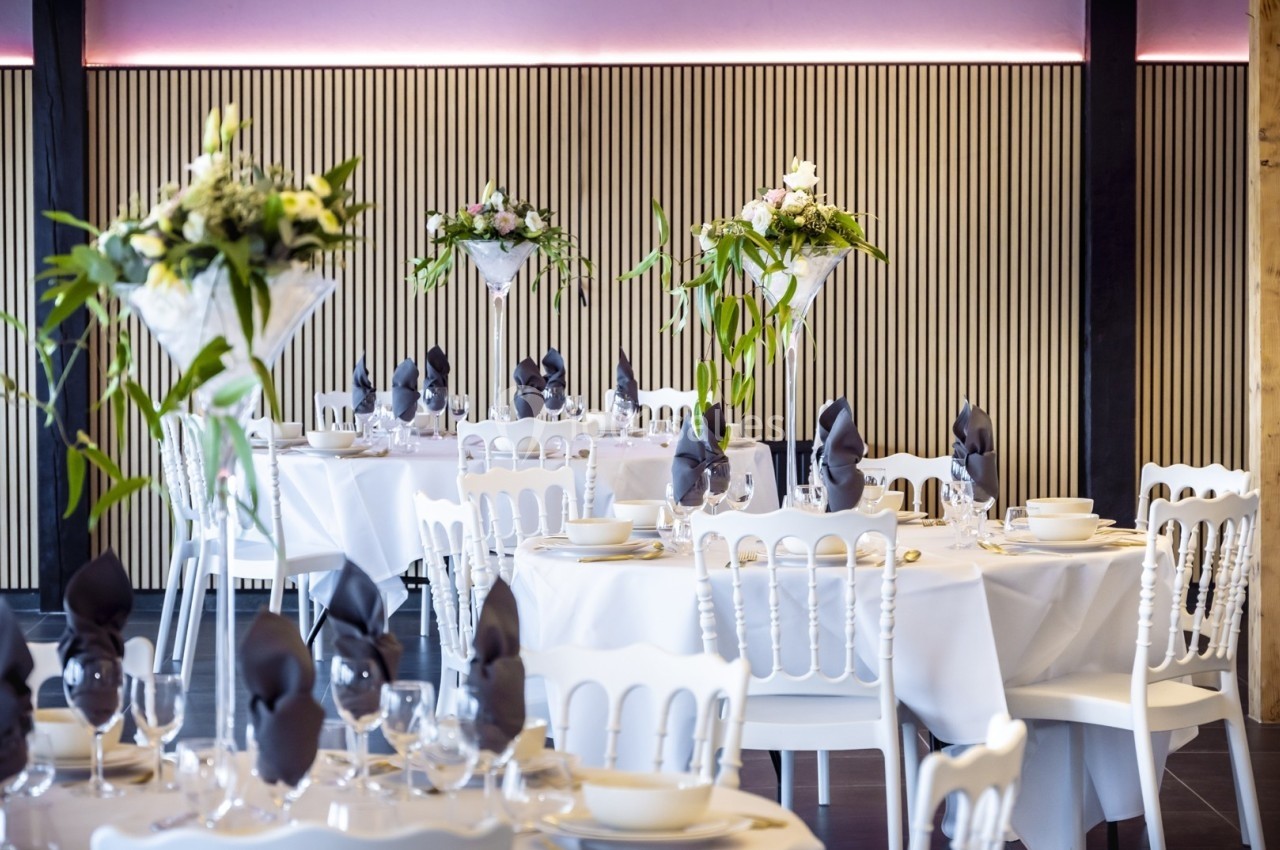 Salle de réception élégante avec tables dressées, nappes blanches, serviettes pliées et décorations florales.