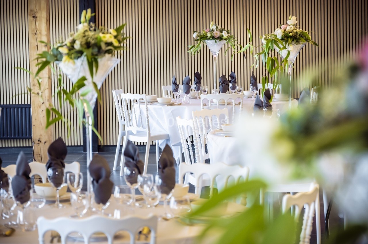 Salle de réception décorée avec des tables dressées, nappes blanches, serviettes pliées et centres de table fleuris.
