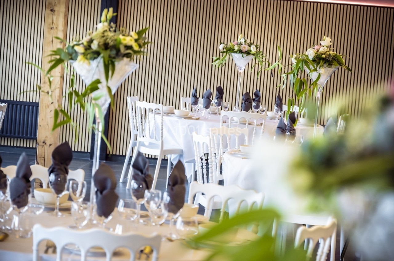 Salle de réception décorée avec des tables dressées, nappes blanches, serviettes pliées et arrangements floraux élégants.