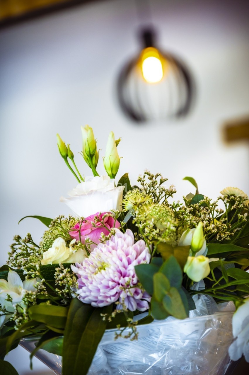Bouquet de fleurs variées avec des roses blanches, un chrysanthème rose et des feuillages, éclairé par une lampe suspendue.