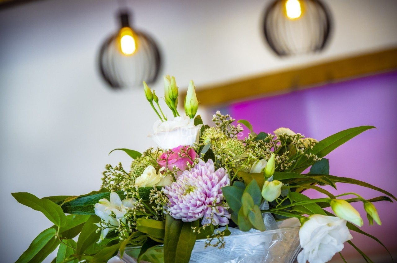 Bouquet de fleurs variées avec des tons pastel, posé dans un intérieur éclairé par des suspensions lumineuses.