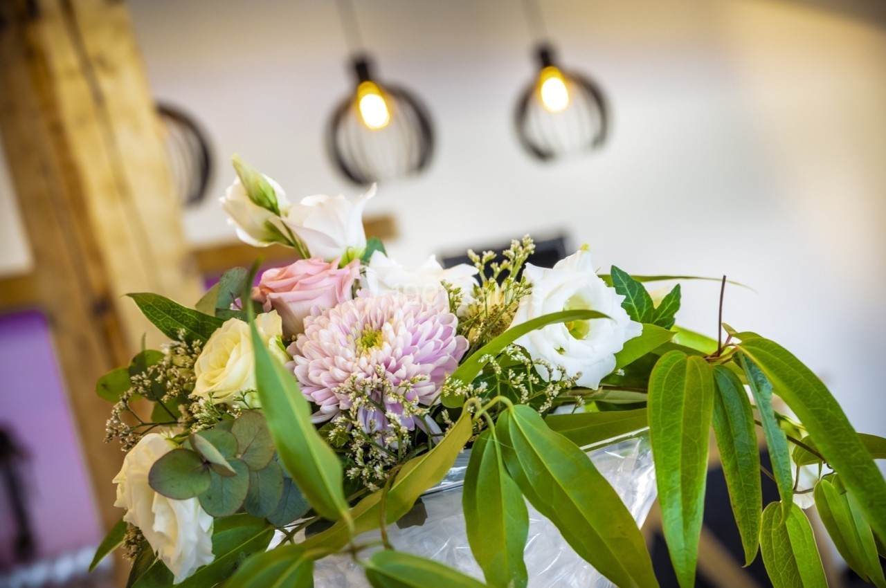 Bouquet de fleurs composé de roses, chrysanthèmes et feuillage, posé dans un intérieur lumineux avec des lampes suspendues.