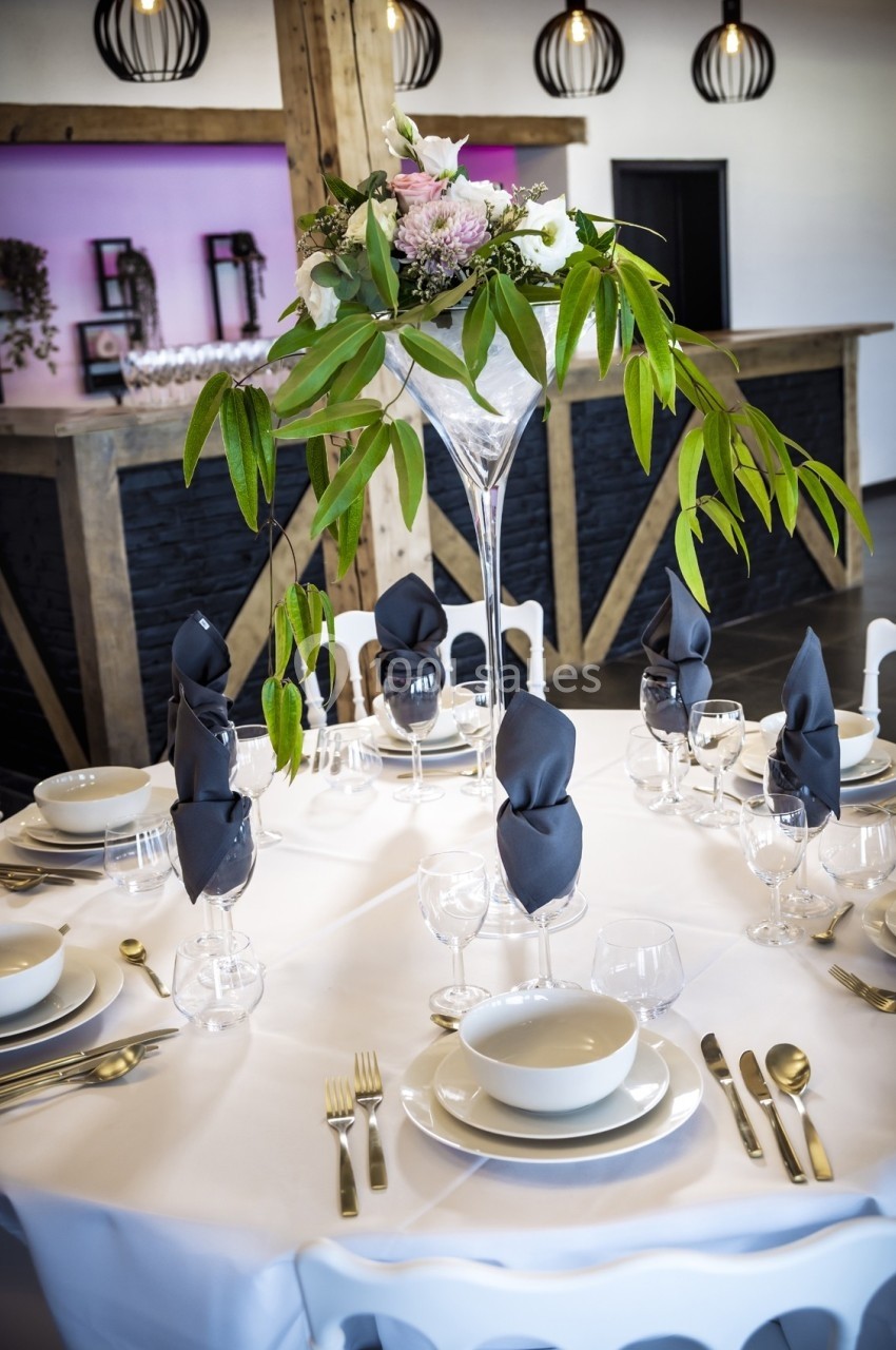 Table dressée avec vaisselle blanche, serviettes noires pliées et centre de table floral dans un vase haut.