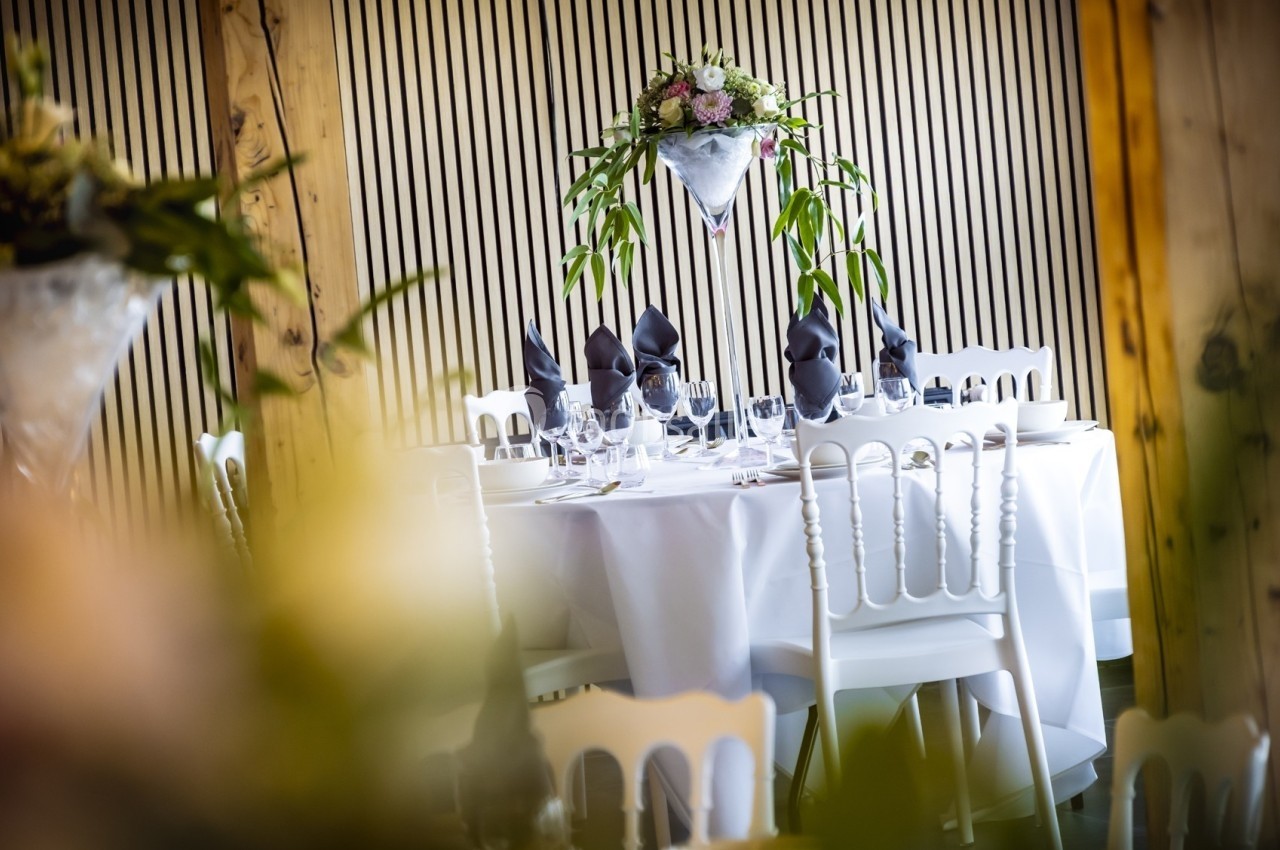 Table élégamment dressée avec nappes blanches, serviettes noires pliées et centre de table floral.