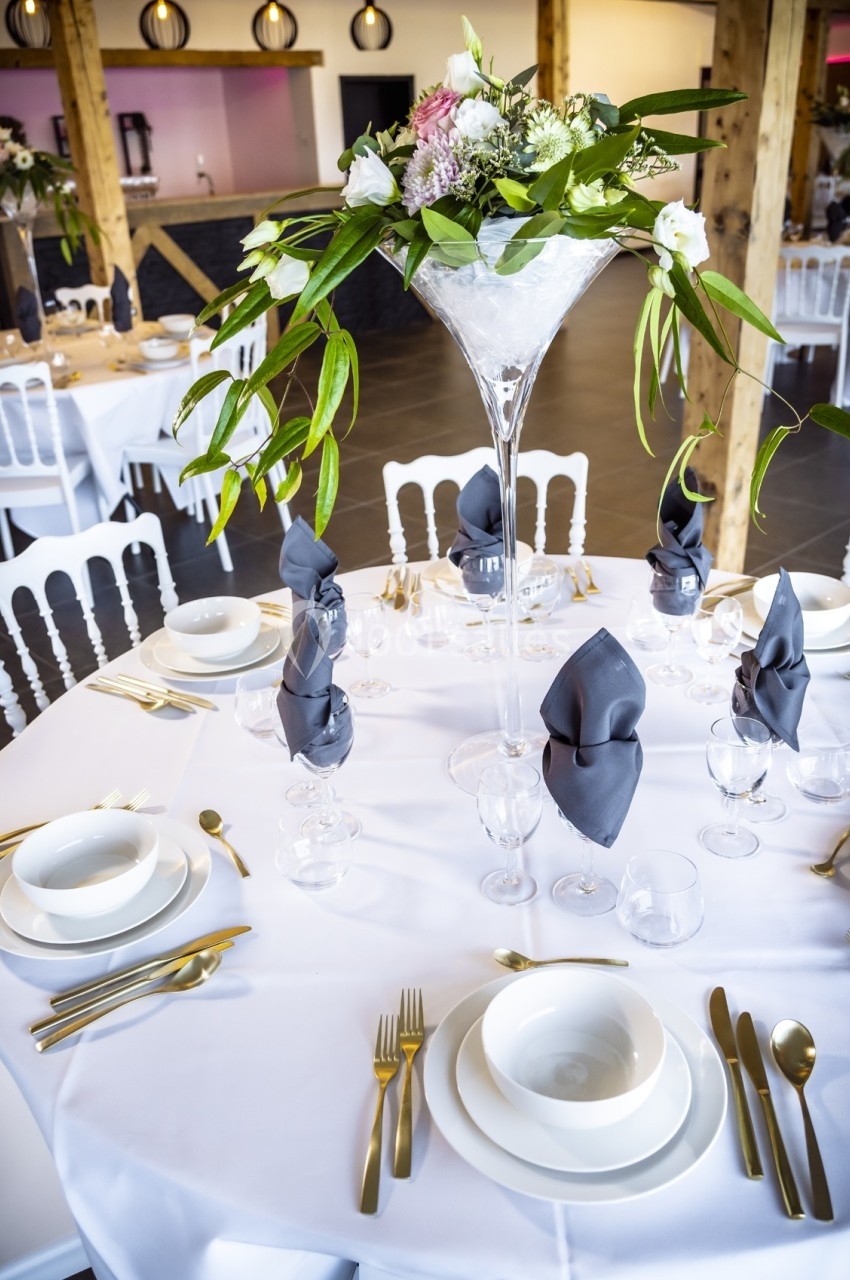 Table dressée avec vaisselle blanche, couverts dorés, serviettes grises pliées et centre de table floral élégant.