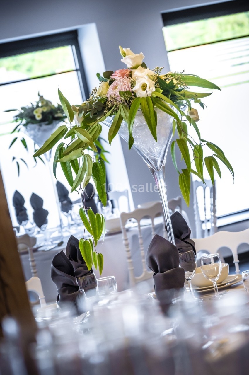 Centre de table floral dans un vase haut, entouré de serviettes pliées sur une table dressée élégamment.