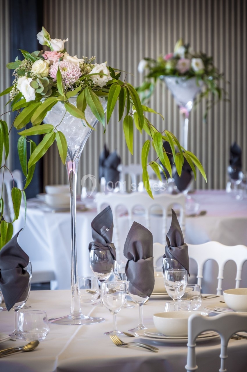 Centre de table floral avec feuilles vertes et fleurs pastel sur une table dressée avec serviettes grises pliées.
