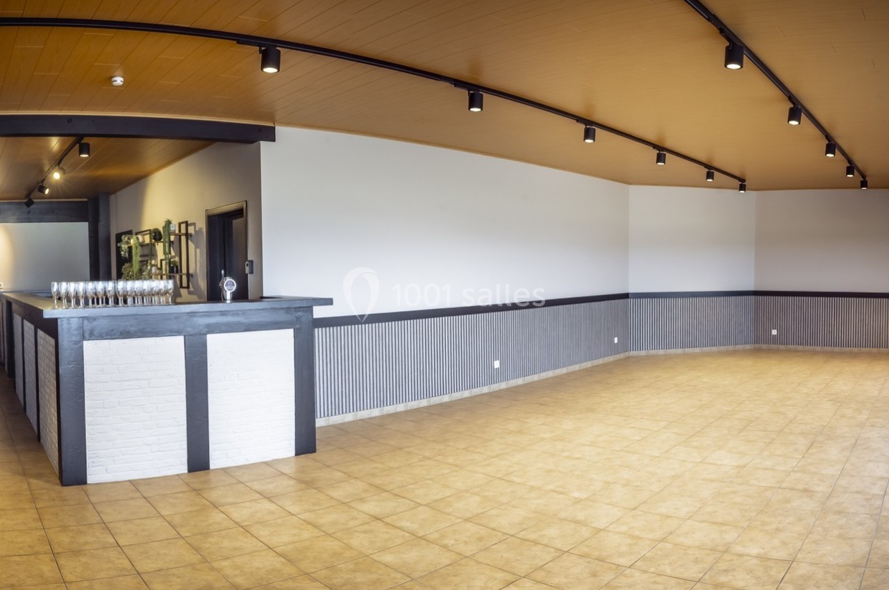 Salle vide avec un bar en bois et briques blanches, éclairage au plafond, sol carrelé et murs clairs.