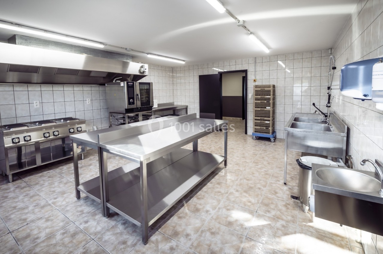 Cuisine professionnelle avec équipements en inox, carrelage au sol et aux murs, éclairage fluorescent.