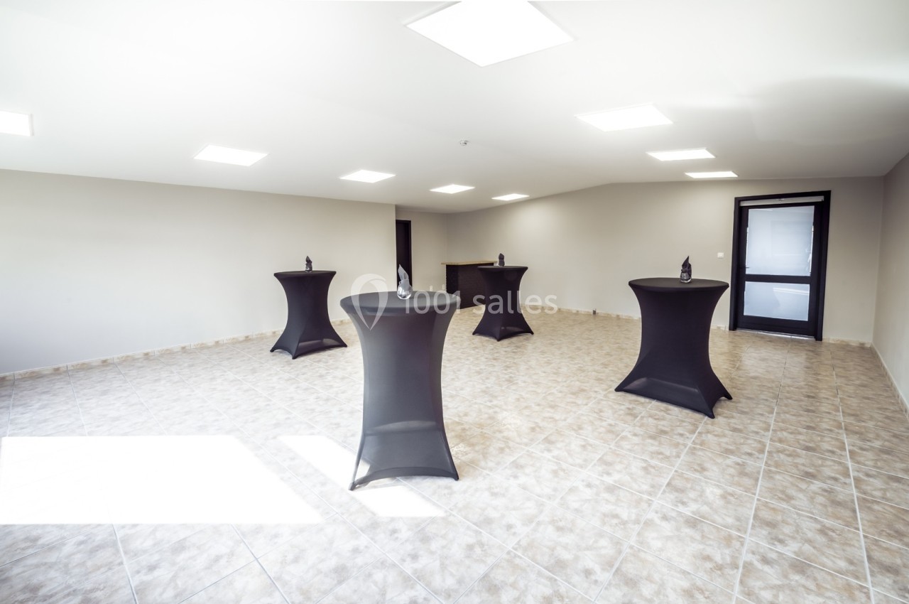 Salle vide avec sol carrelé, tables hautes noires et éclairage au plafond.