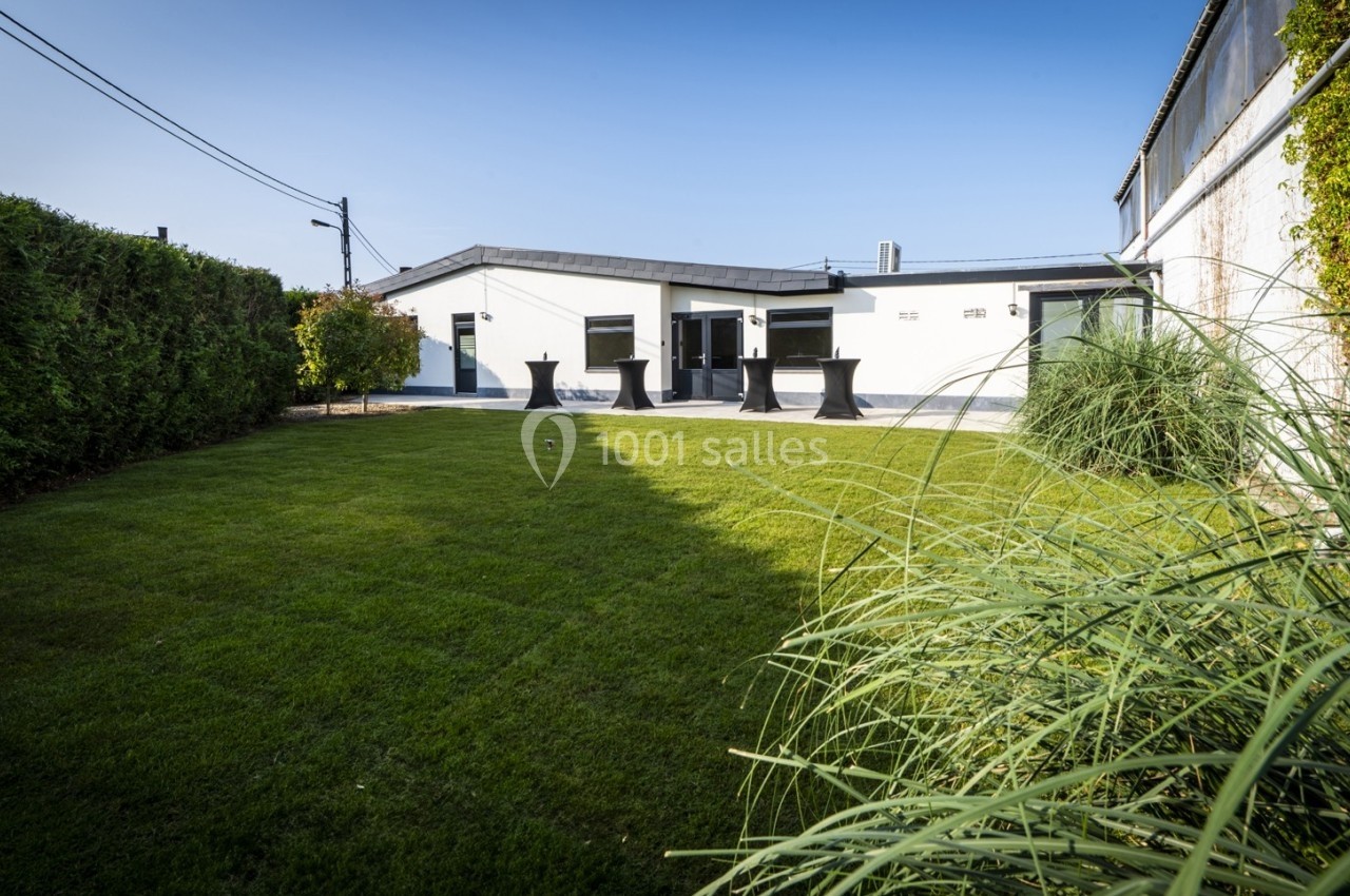 Jardin avec pelouse bien entretenue, bordé de haies et donnant sur une maison moderne avec terrasse.