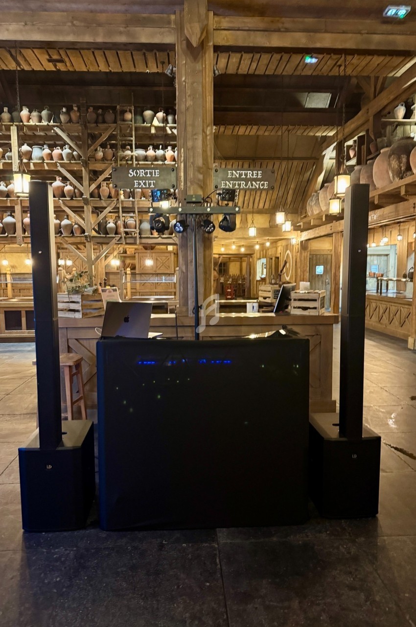 Poste de DJ installé dans une salle en bois avec des jarres décoratives sur des étagères en arrière-plan.