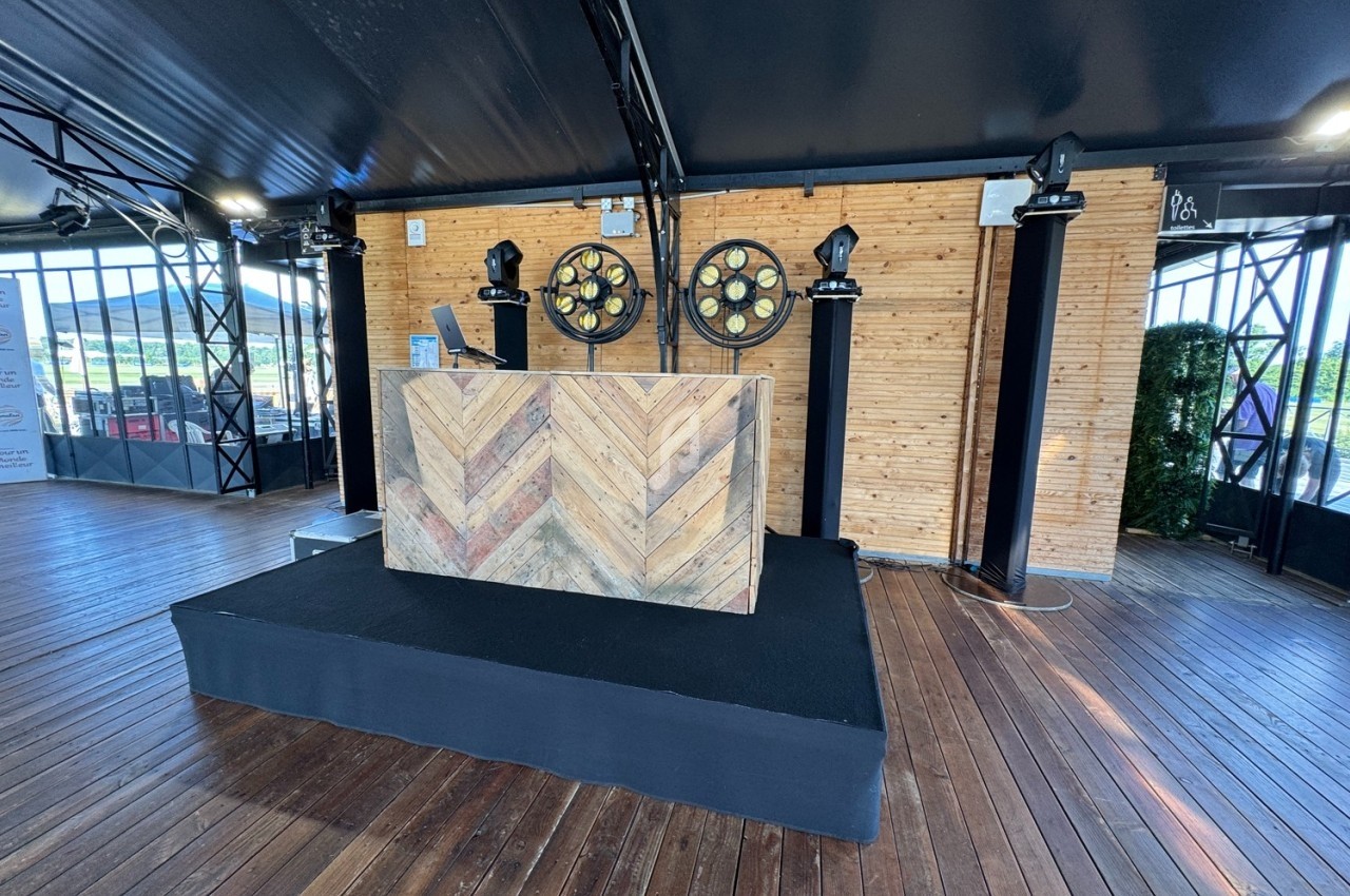 Scène en bois avec un pupitre décoratif, deux projecteurs circulaires et un fond de murs en bois clair.