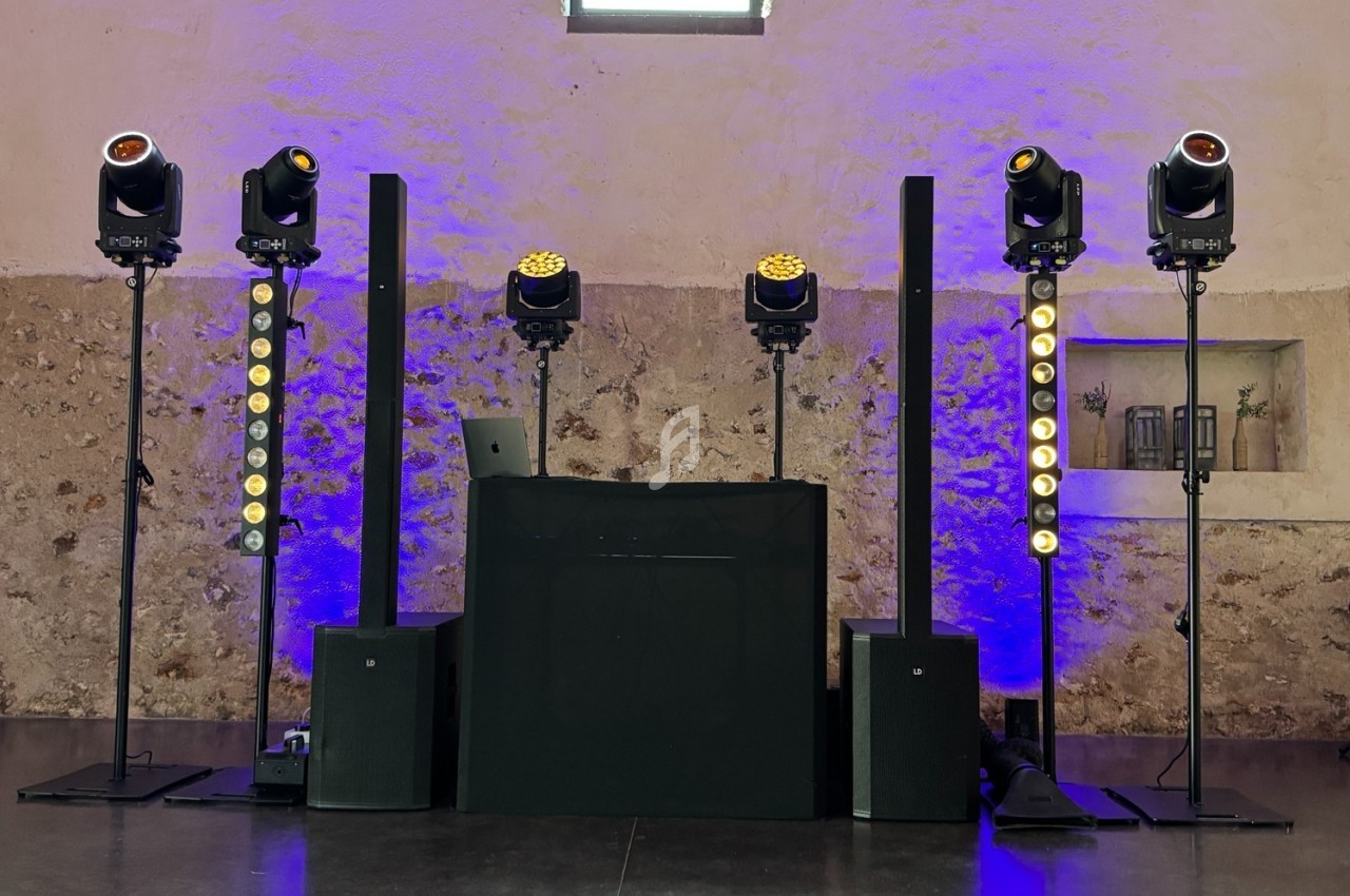 Installation de matériel de sonorisation et d'éclairage avec projecteurs et enceintes dans une salle en pierre.