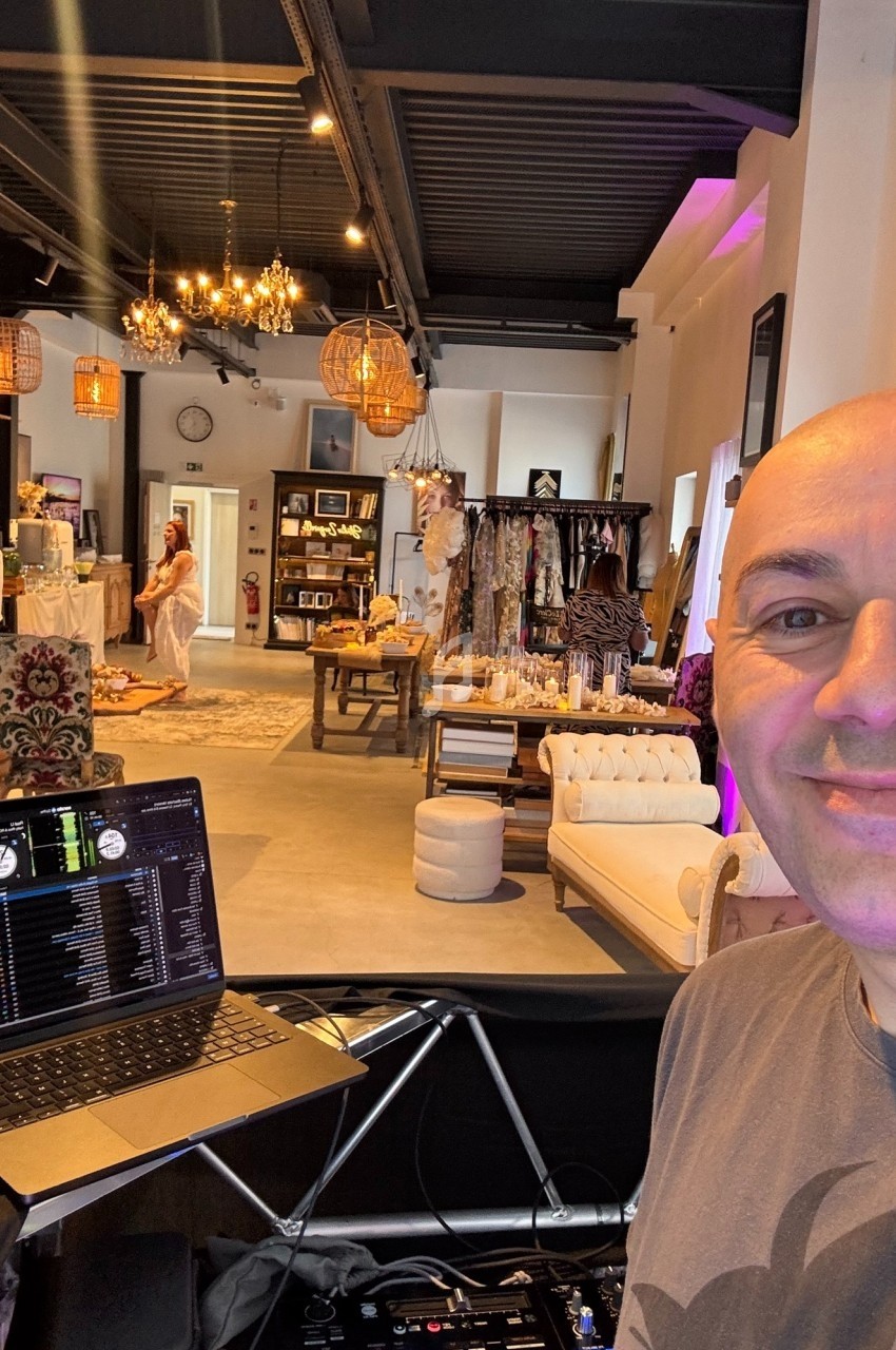 Un homme souriant devant un ordinateur portable dans une boutique élégante avec vêtements et décorations.