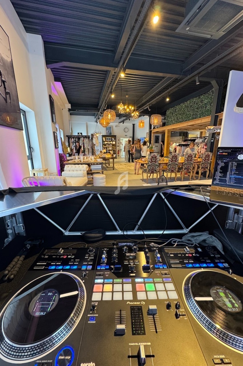 Vue depuis une table de mixage DJ dans un espace intérieur moderne avec des vêtements exposés et des personnes en arrière…