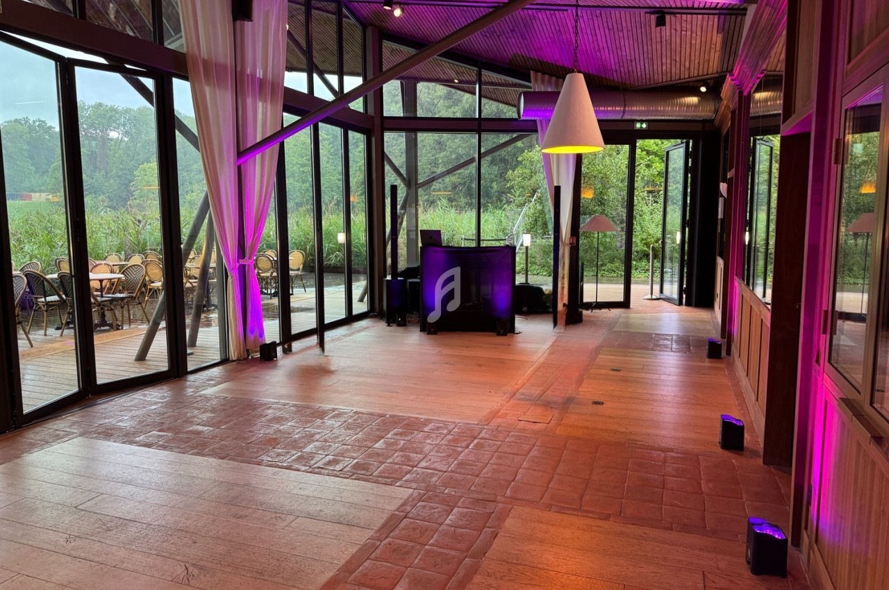 Salle lumineuse avec grandes baies vitrées, vue sur une terrasse et un jardin, éclairage intérieur violet.