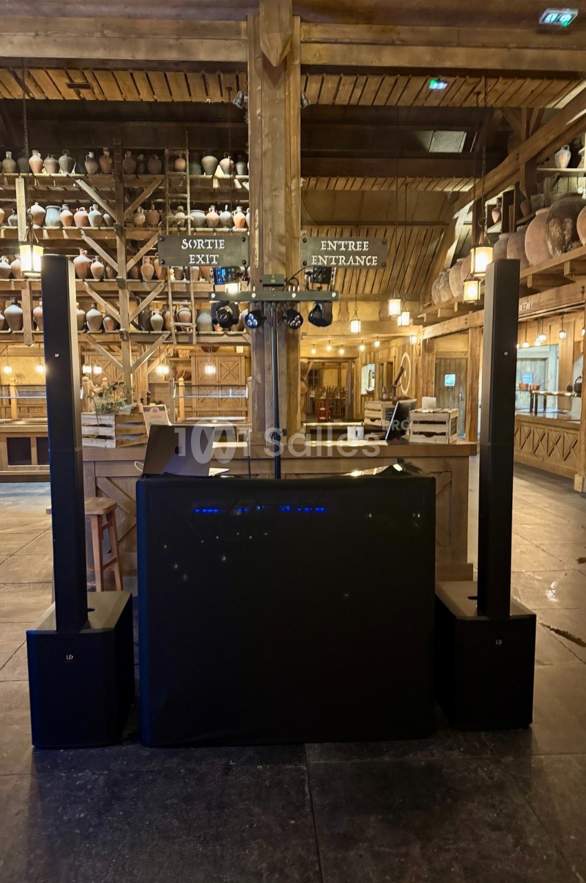 Poste de DJ installé dans une salle en bois avec des colonnes sonores et des éclairages suspendus.
