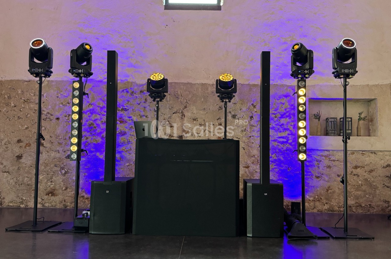 Installation de matériel de sonorisation et d'éclairage avec projecteurs et enceintes dans une salle en pierre.