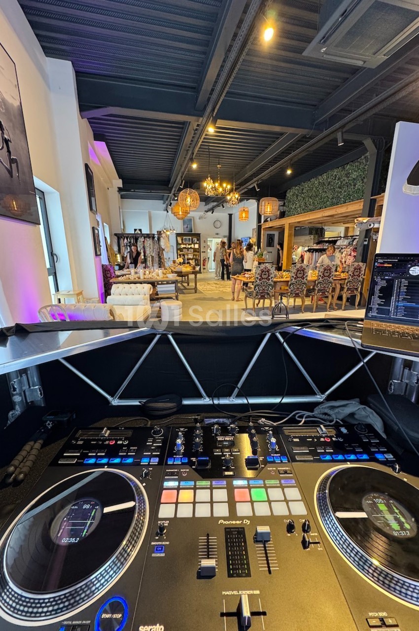 Vue depuis une table de mixage DJ dans un espace intérieur moderne avec des vêtements exposés et des personnes en arrière…