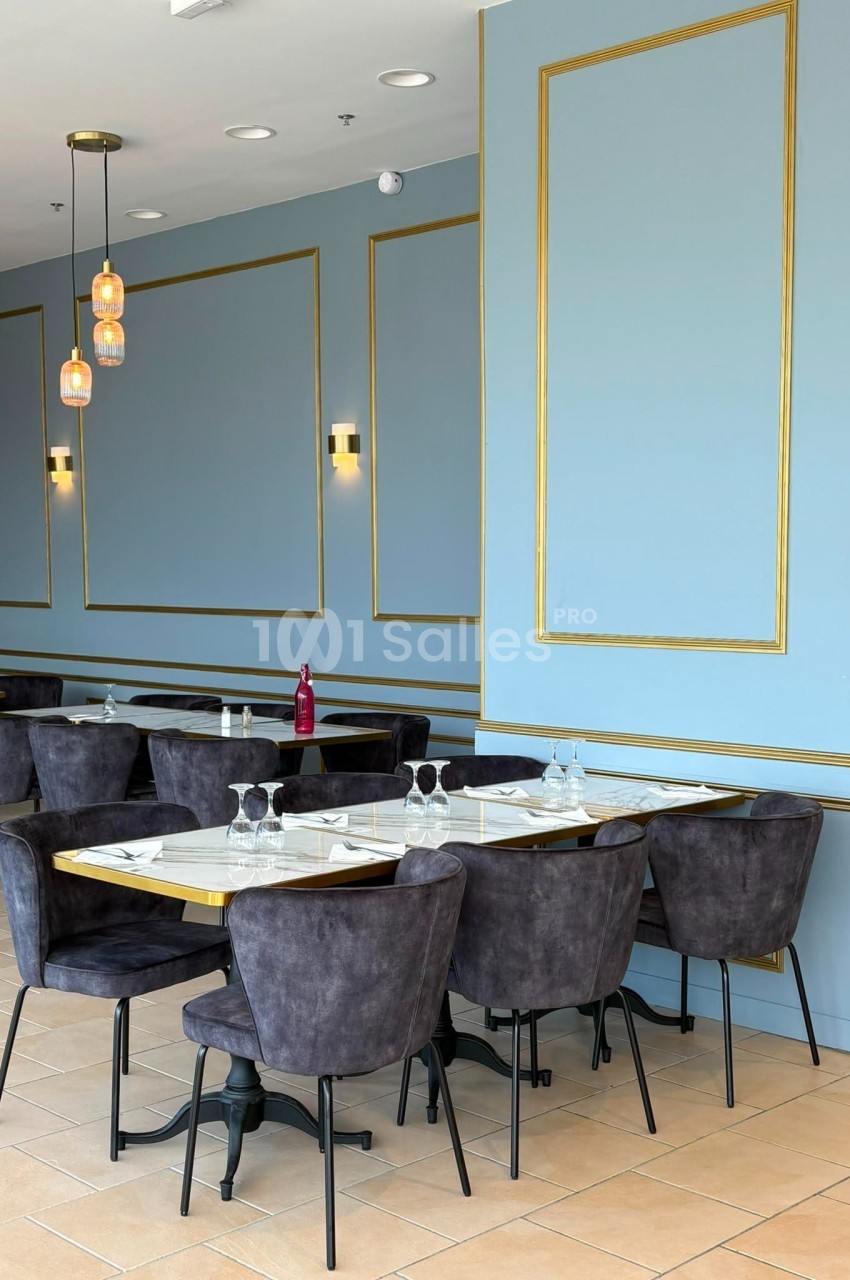 Salle de restaurant élégante avec murs bleu clair, moulures dorées, tables dressées et chaises en velours gris.