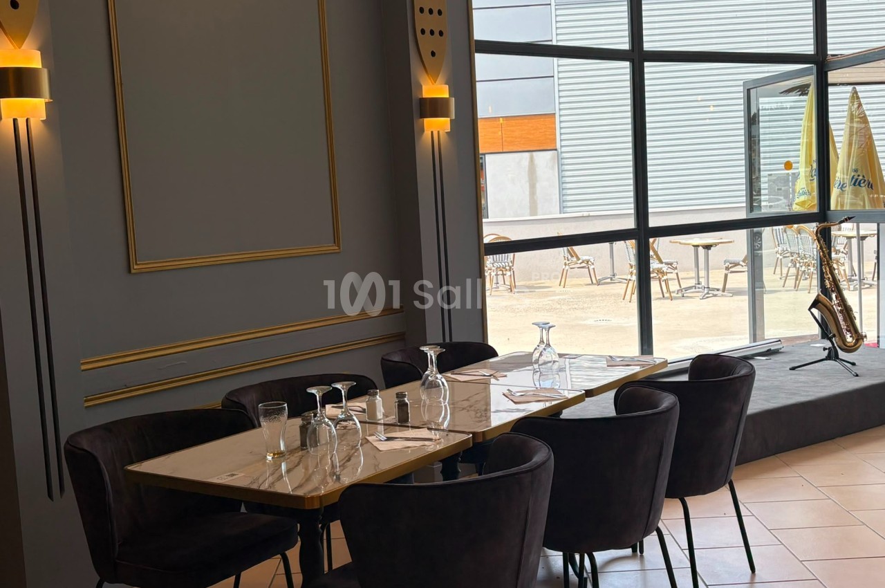 Salle de restaurant élégante avec table dressée, chaises noires et vue sur une terrasse extérieure ensoleillée.