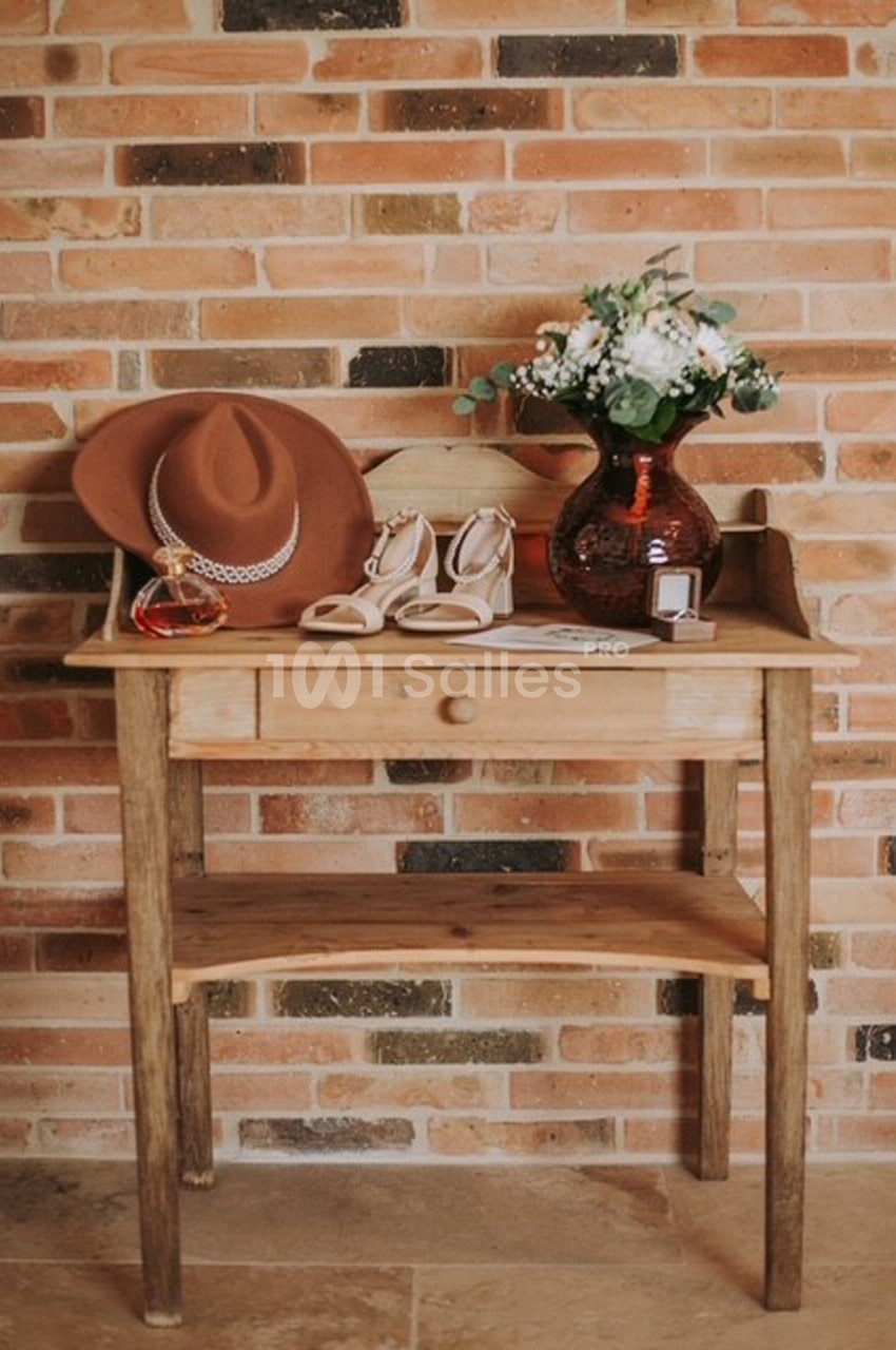 Table en bois contre un mur de briques, décorée avec un chapeau, un vase de fleurs, des chaussures et des accessoires.