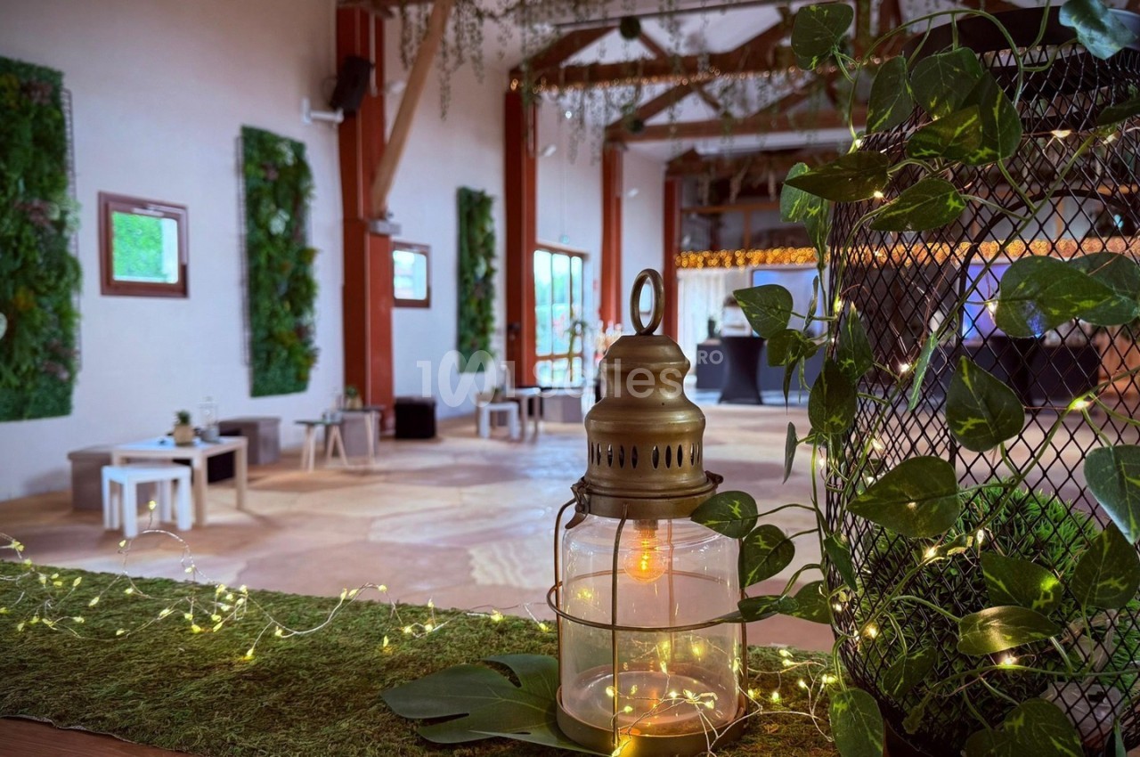 Salle décorée avec des plantes, guirlandes lumineuses et une lanterne en premier plan sur une table recouverte de mousse.