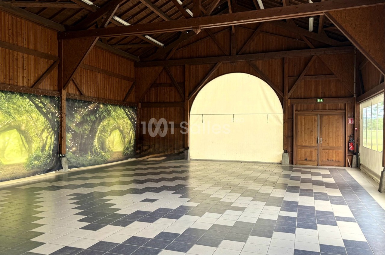 Salle vide avec charpente en bois, murs décorés de fresques forestières et sol carrelé à motifs géométriques.