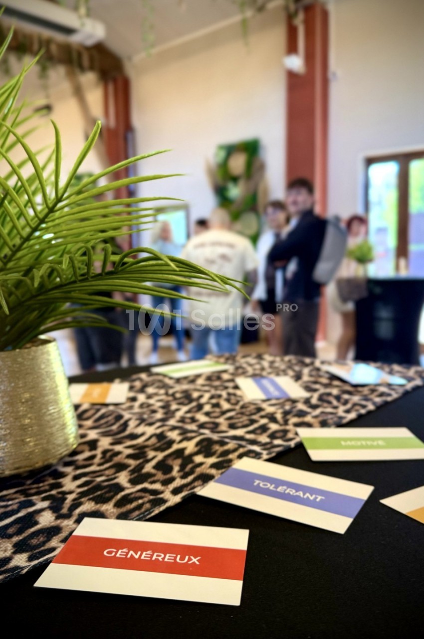 Cartes avec des adjectifs sur une table à motif léopard, dans une salle avec des plantes et des personnes en arrière-plan.