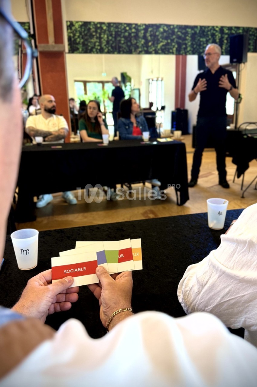 Une personne tient des cartes colorées pendant une présentation interactive dans une salle avec un groupe de participants.
