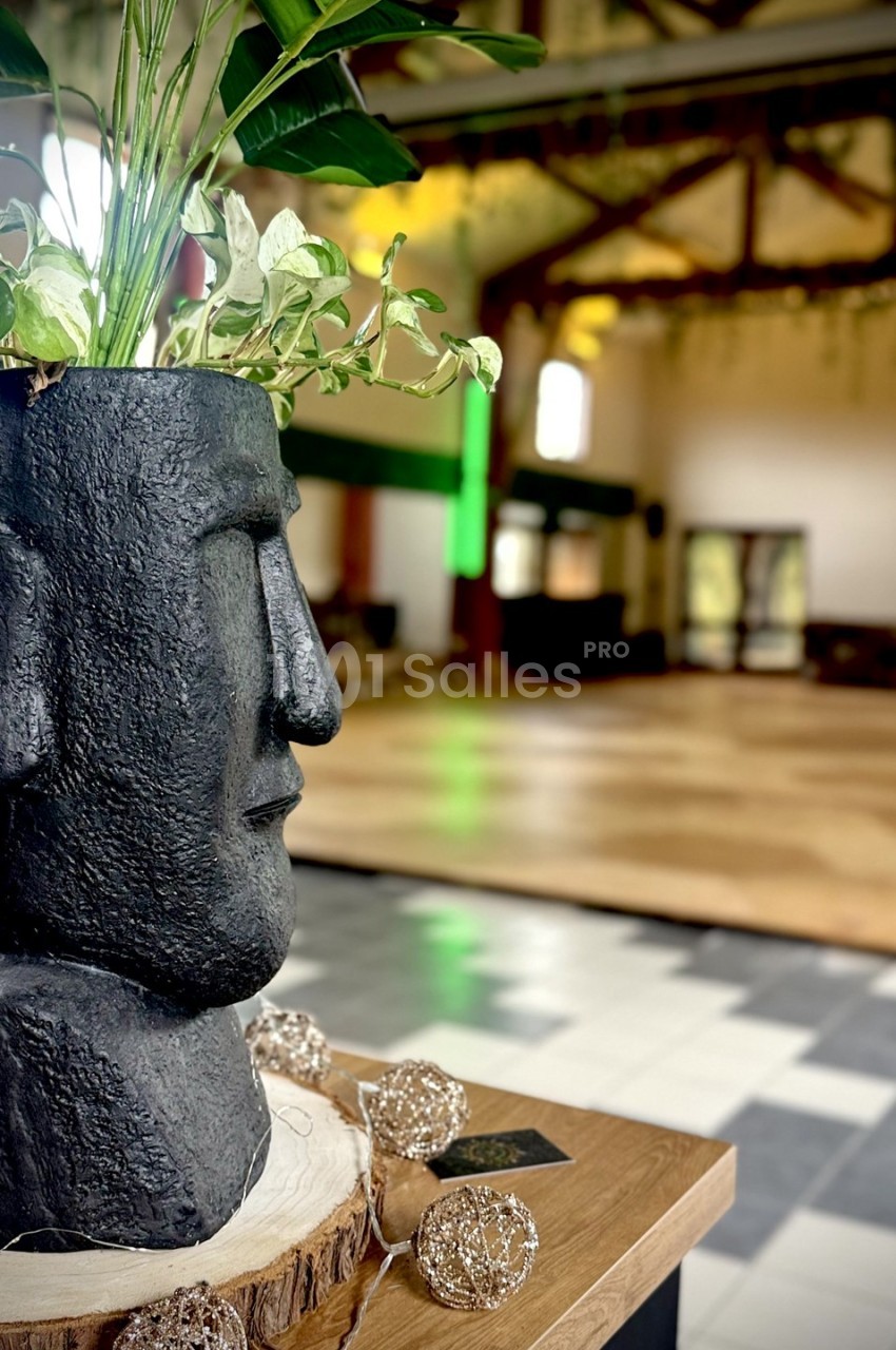 Pot de fleurs en forme de tête sculptée, posé sur une table en bois, dans une grande salle lumineuse.